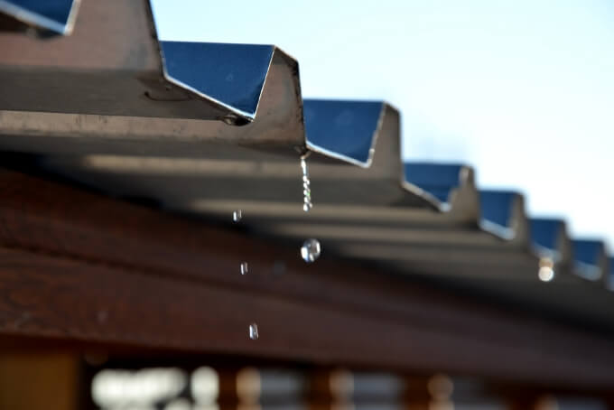 錆によって穴が開きやすく、錆止め塗装をせずに放置するとすぐに雨漏りや崩落が発生してしまう薄い鉄の屋根から滴る雨水のイメージ