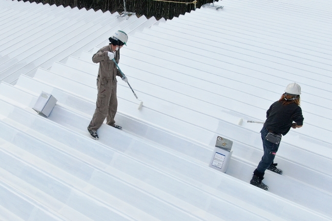 屋根等に塗装するだけで建物内が涼しくなる特殊な塗料、遮熱塗料ミラクールの開発者が開発した塗料を屋根に塗布し、塗りやすさに満足している職人のイメージ